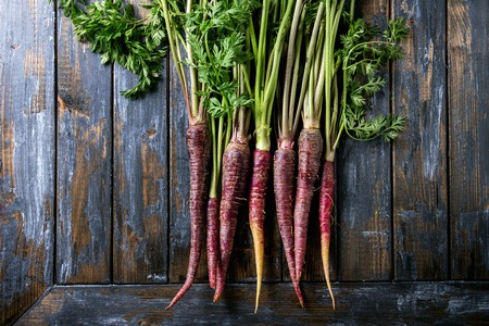 Bundle of raw organic purple carrot with green top haulm over old wooden plank background. Top view with copy space. Food background.の写真素材
