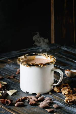 Vintage mug of hot chocolate, decor with nuts, caramel, spices. Ingredients above. Chopped dark and white chocolate, cocoa beans, anise over old wooden table. Dark rustic styleの写真素材