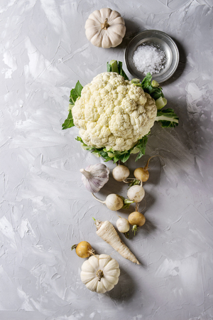 Variety of white vegetables raw organic cauliflower, pumpkins, garlic, parsnip and radish with plate of sea salt over gray texture background. Top view with space. Healthy eating conceptの写真素材