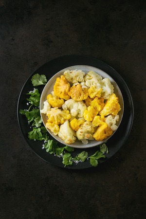 White and yellow cauliflower gratin served on black ceramic plate with coriander leaves over dark texture background. Flat lay with copy space. Restaurant menu concept.の写真素材