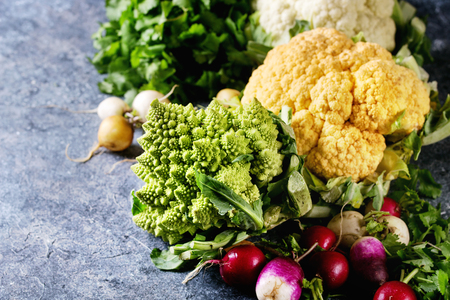 Variety of fresh raw organic colorful cauliflower, cabbage romanesco and radish with bundle of coriander over dark texture background. Close up with space. Healthy eating conceptの写真素材