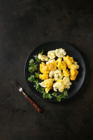 White and yellow cauliflower gratin served on black ceramic plate with coriander leaves, textile napkin and cutlery over dark texture background. Flat lay with copy space. Restaurant menu conceptの写真素材