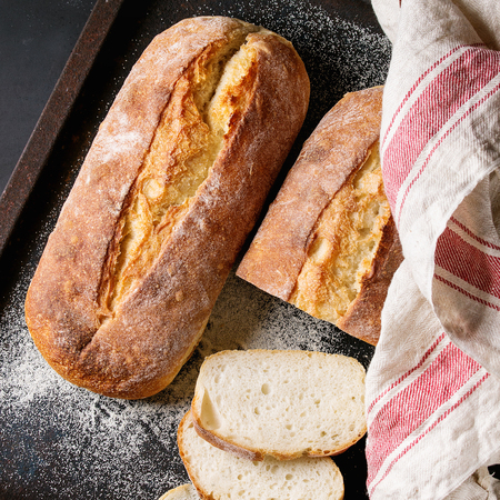 Whole and slice homemade white wheat bread with wheat flour and kitchen towel on old black oven tray as background. Top view. Square imageの写真素材