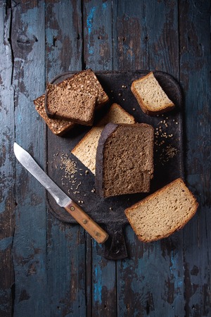 Variety loaves of sliced homemade rye bread whole grain and seeds with knife on black cutting board over old dark wooden background. Top view, space. Healthy eatingの写真素材