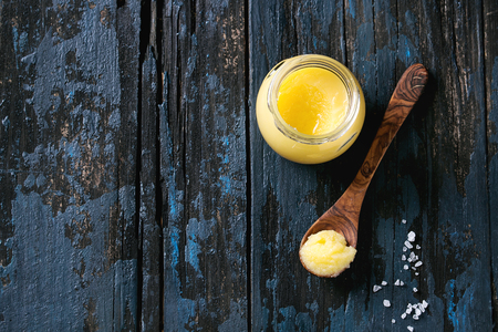 Glass of salted drawn ghee butter standing with wood spoon and sea salt over old dark blue wooden background. Healthy eating. Top view, copy spaceの写真素材