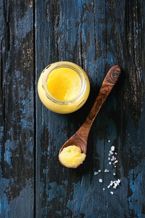 Glass of salted drawn ghee butter standing with wood spoon and sea salt over old dark blue wooden background. Healthy eating. Top view, copy spaceの写真素材