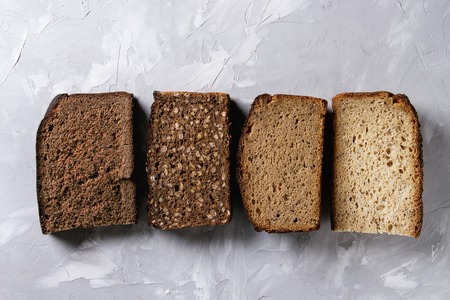 Variety loaves of sliced homemade rye bread whole grain and seeds over gray texture background. Top...