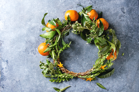Christmas wreath with clementines tangerines and green branches over blue texture background. Top view, copy space. New Year cards and decorations.の写真素材
