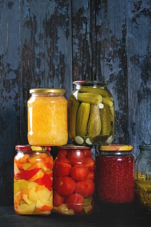 Variety glass jars of homemade pickled or fermented vegetables and jams in row with old dark blue wooden plank background. Seasonal preserves.の写真素材