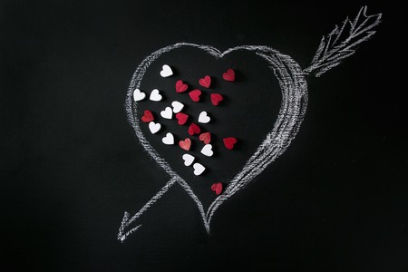 White and red decorative hearts inside drawn by chalk heart shape over black background. St...