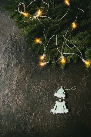 Christmas lights garland on green fir tree branches and decor toy elf clothing over dark texture background. Christmas holiday mood card. Top view with spaceの写真素材
