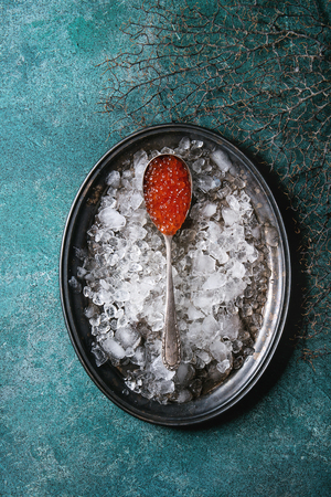 Spoon of red caviar on vintage metal tray with ice over turquoise texture background. Top view, spaceの写真素材