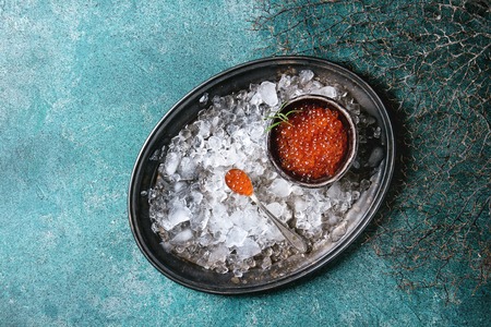 Bowl of red caviar on vintage metal tray with ice over turquoise texture background. Top view, spaceの写真素材