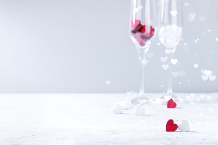 Love Valentine day greeting card with two empty champagne glasses and wooden hearts over white gray background. Copy space. Selective focus