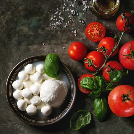 Ingredients for italian caprese salad. Mozzarella balls, buffalo in metal vintage plate, tomatoes, basil leaves, olive oil with vinegar over dark background. Top view with space. Rustic style. Square imageの写真素材