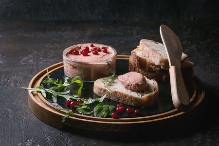 Chicken homemade liver paste or pate with sliced whole grain bread, wood knife, cranberries, green salad served in glass jar on wooden slate serving board over dark texture background. Copy spaceの写真素材