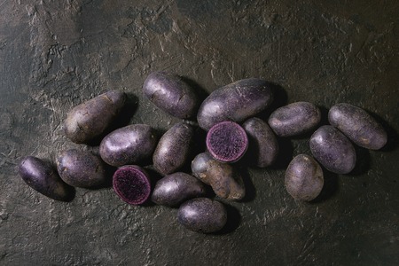 Raw purple uncooked organic potatoes named prunelle, whole and slice over dark texture background. Top view, copy spaceの写真素材