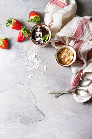 Chocolate and vanilla caramel mug cakes from microwave with fresh strawberries and kitchen towel over grey texture background. Top view, spaceの写真素材