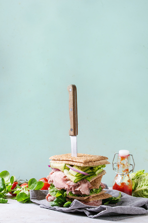 Beef and vegetables sandwiches with sliced meat, cucumber, green salad, rye whole grain bread in stack with knife on textil napkin over grey green pin-up style background. Ingredients aboveの写真素材