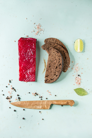 Piece of beetroot marinated salted salmon with sliced rye bread, pink salt, pepper, lime and wooden knife over light green pin-up style background. Top view, space. Food knollingの写真素材