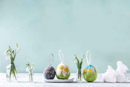 Set of craft felting Easter eggs with blooming flower sakura and green grass decor standing with spring snowdrops bouquet in glass bottle on grey table. Easter decoration and gifts. Copy spaceの写真素材