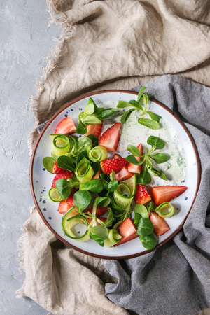 Spring summer diet salad with strawberries, cucumber, green field salad and yogurt mint sauce served in blue plate over different cloth background. Top view, spaceの写真素材