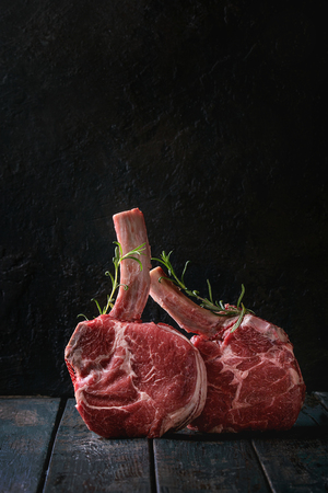 Raw uncooked black angus beef tomahawk steaks on bones served with rosemary over dark wooden plank table. Rustic style. Close upの写真素材