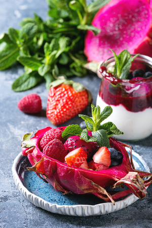 Vegan fruit salad with berries and mint served in pink dragon fruit with ingredients above on ceramic plate over blue texture background. Close up. Healthy eatingの写真素材