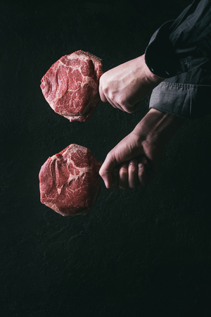 Man's hands holding raw uncooked black angus beef tomahawk steaks on bones over dark background. Rustic style. Toned imageの写真素材