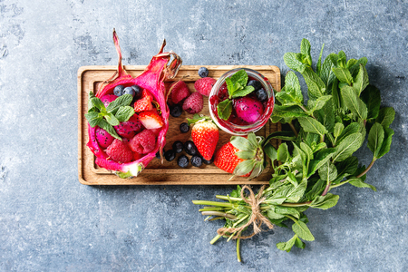 Vegan fruit salad with berries and mint served in pink dragon fruit with ingredients above on wooden serving board over blue texture background. Top view, space. Healthy eatingの写真素材