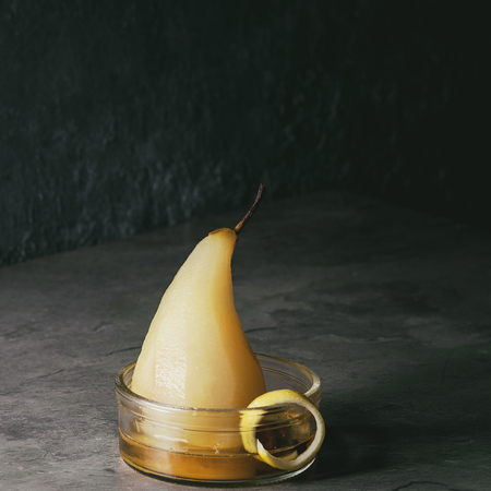 Traditional dessert poached pear in white wine served in glass bowl with syrup and lemon zest over gray texture table. Square imageの写真素材
