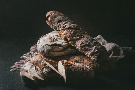Variety of loafs fresh baked artisan rye and whole grain bread on linen cloth over dark brown texture background. Copy space.の写真素材