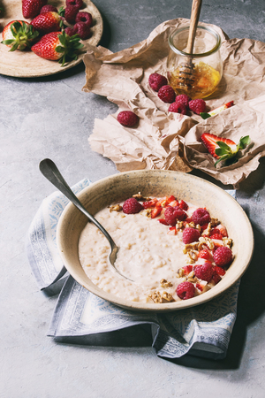 Sweet rice porridge pudding in ceramic plate with berries strawberry and raspberry, walnuts, honey and mug of milk on crumpled paper over grey kitchen table. Toned imageの写真素材