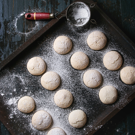 Homemade almond cookies with sugar powder, with vintage sieve, on old oven tray over dark blue wooden table. Dark rustic style. Top view, space. Square imageの写真素材