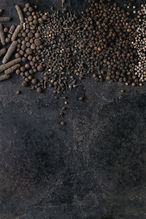 Variety of different black peppers allspice, pimento, long pepper, monks pepper, peppercorns over old black iron texture surface. Food background. Top view, space.の写真素材
