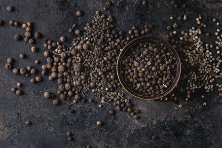 Variety of different black peppers allspice, pimento, monks pepper, peppercorns and ground powder in...