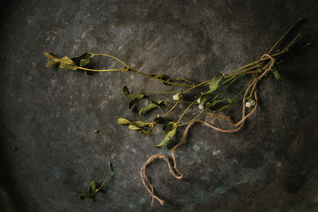 Traditional Christmas plant mistletoe branches with berries and thread over old dark metal background. Top view, spaceの写真素材