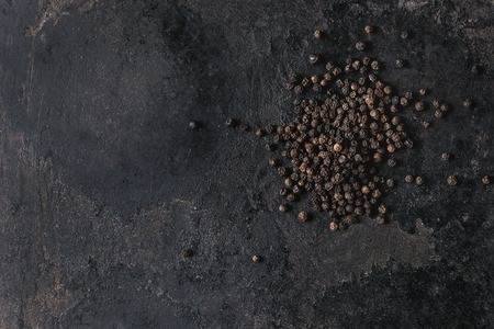 Heap of black pepper peppercorns over old black iron texture background. Top view, copy space.の写真素材