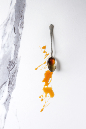 Homemade liquid transparent brown sugar caramel in vintage spoon over white marble background. Flat lay, space.の写真素材