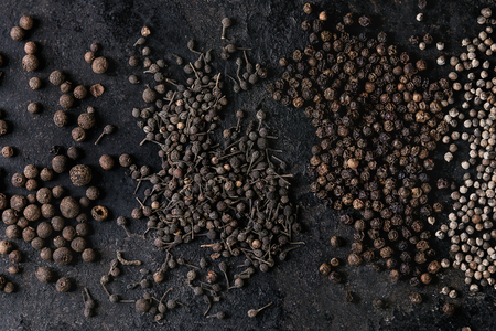 Variety of different black peppers allspice, pimento, monks pepper, peppercorns over old black iron texture surface. Food background. Top view, space.の写真素材