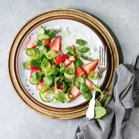 Spring summer diet salad with strawberries, cucumber, green field salad and yogurt mint sauce served in blue plate with cloth napkin over grey texture background. Top view, copy spaceの写真素材