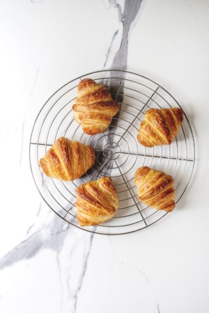 Homemade croissant on cooling rack over white marble background. Flat lay, space.の写真素材