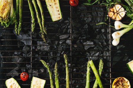 Grilled vegetables green asparagus, garlic, lemon, spring onion, zucchini, cherry tomatoes, salad on bbq grill rack over charcoal. Top view, space. Barbecue conceptの写真素材