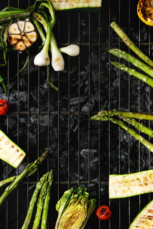 Grilled vegetables green asparagus, garlic, lemon, spring onion, zucchini, cherry tomatoes, salad on bbq grill rack over charcoal. Top view, space. Barbecue conceptの写真素材
