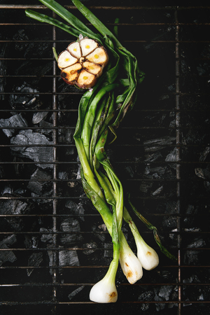 Grilled vegetables spring onion and garlic on bbq grill rack over charcoal. Top view, space. Barbecue conceptの写真素材