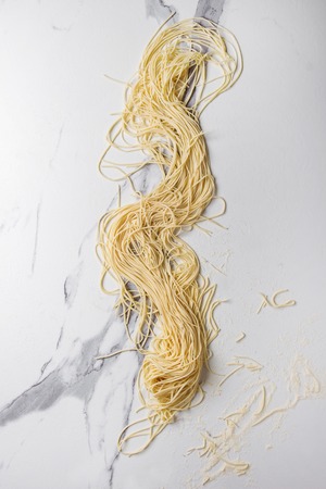 Homemade italian uncooked pasta spaghetti with semolina flour over white marble texture background. Flat lay, space.の写真素材