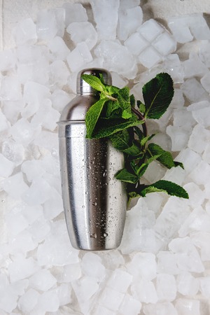 Cocktail making concept. Silver shaker with bundle of fresh mint over crushed ice cubes. Flat lay, space.の写真素材