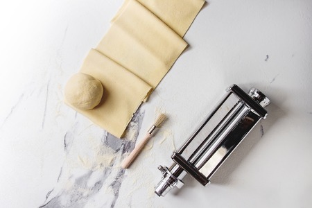 Rolled dough for homemade italian uncooked pasta lasagna from pasta machine maker with semolina flour over white marble texture background. Flat lay, space.の写真素材