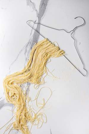 Homemade italian uncooked pasta spaghetti dried on clothes hanger over white marble texture background. Flat lay, space.の写真素材