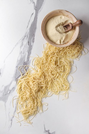 Homemade italian uncooked pasta spaghetti with bowl of semolina flour over white marble texture background. Flat lay, space.の写真素材